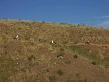 Foothill with ATV riders and others using trail with blue sky.