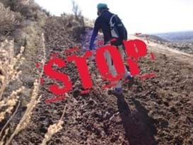 Mountain biker is riding uphill on a muddy trail. The word STOP is written over the image in big red letters.